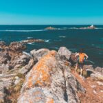 Vue panoramique d'une plage secrète en Bretagne, entourée de falaises et de verdure.